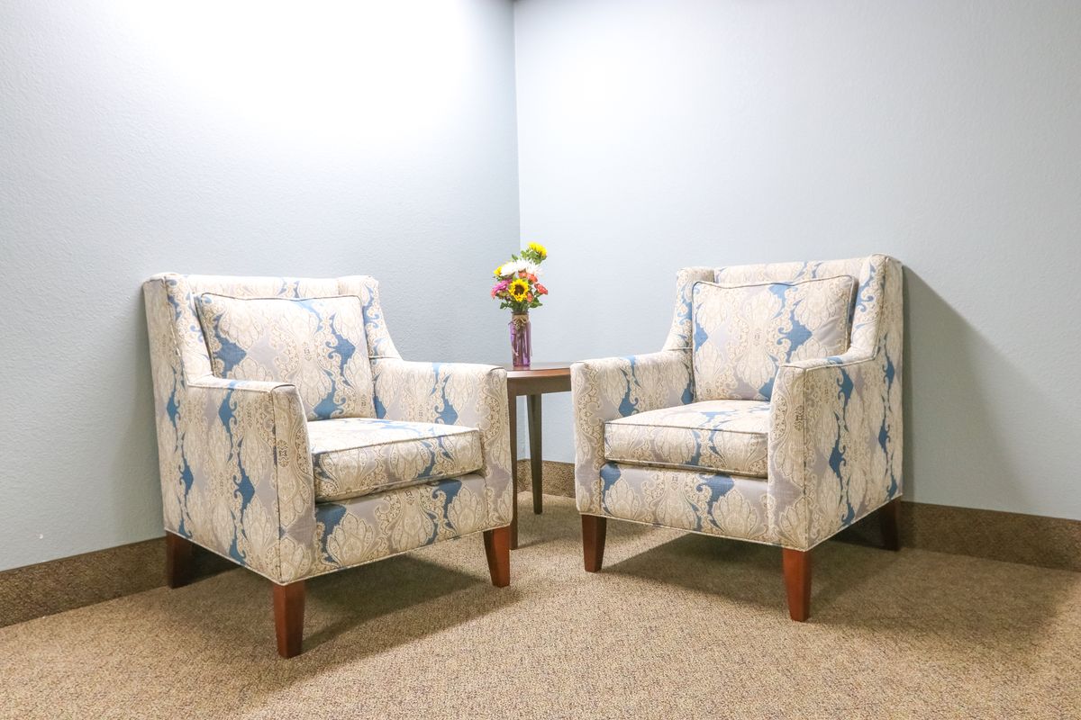 A cozy corner with two patterned armchairs and a small table adorned with flowers.