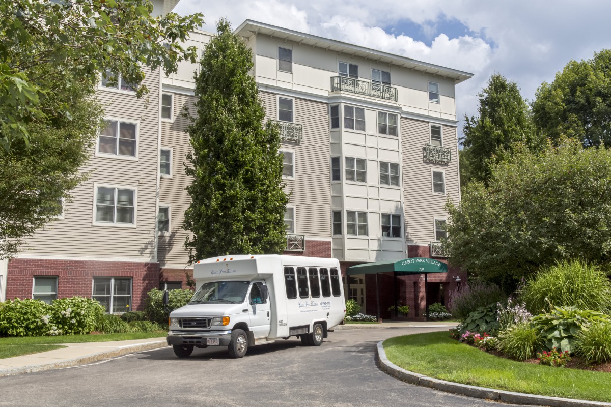 A shuttle bus parked in front of a multi-story residential building surrounded by trees.