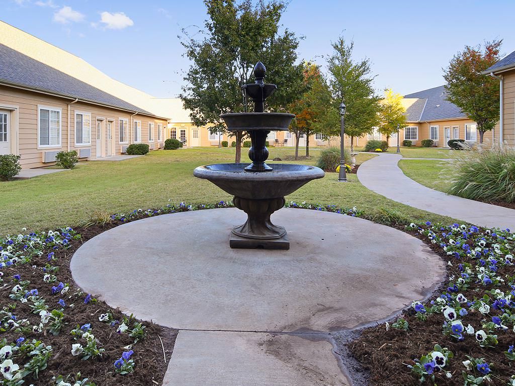 A fountain in a landscaped courtyard with a paved walkway and surrounding buildings.