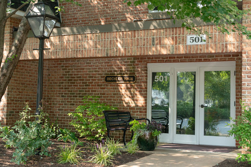 A welcoming entrance to a brick building surrounded by lush greenery and seating.