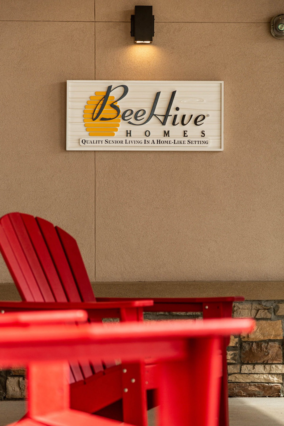 A sign for BeeHive Homes with red outdoor chairs in the foreground.