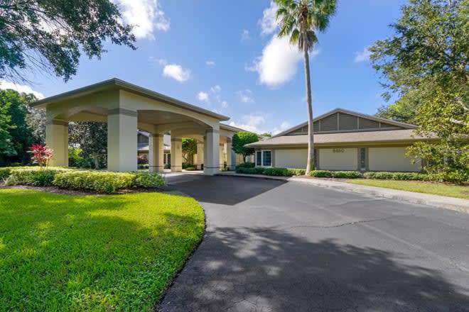 A modern residential building with a covered driveway, surrounded by well-maintained landscaping and a tall palm tree on a bright sunny day.