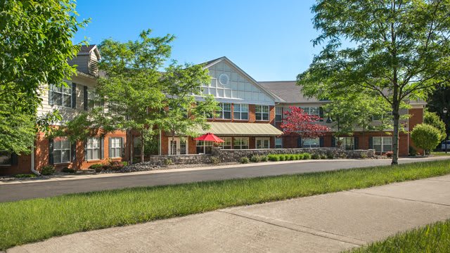 A well-maintained residential building with lush landscaping and a sidewalk under a clear blue sky.