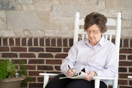 An elderly woman sitting in a rocking chair, focused on writing something down.
