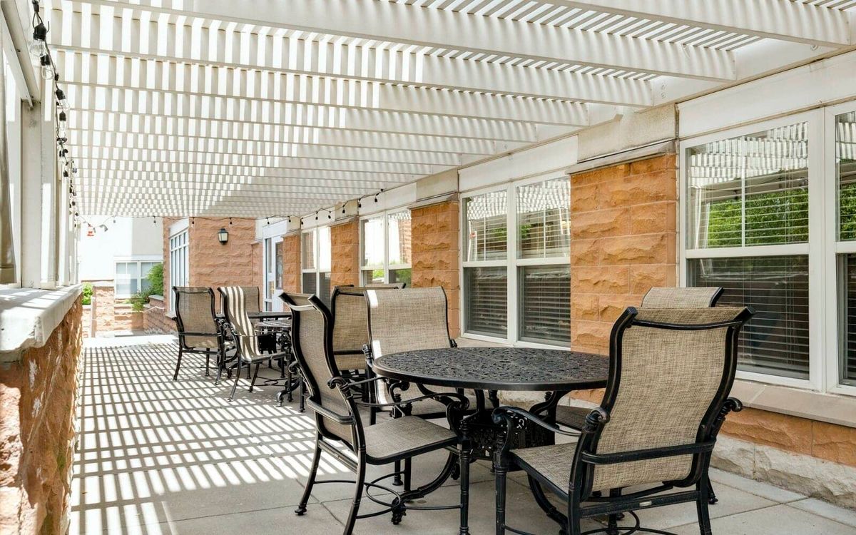 A sunlit outdoor patio area with tables and chairs under a pergola.