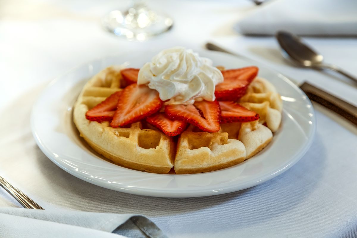 A delicious waffle topped with fresh strawberries and whipped cream served on a white plate.