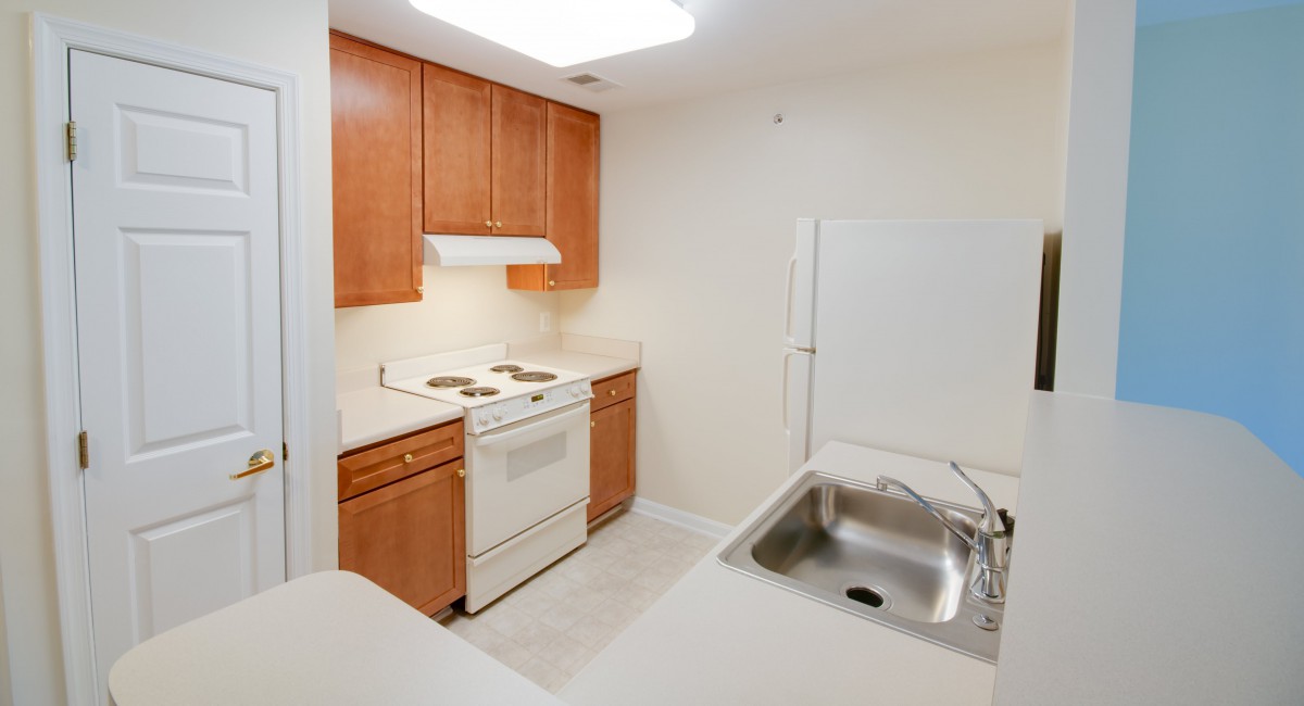 A simple kitchen interior with wooden cabinets, a stove, and a sink.