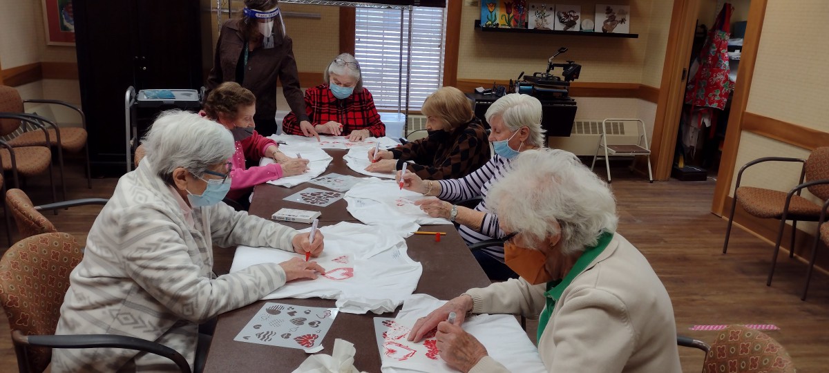 A group of seniors engaging in a crafting activity at a table, wearing masks.