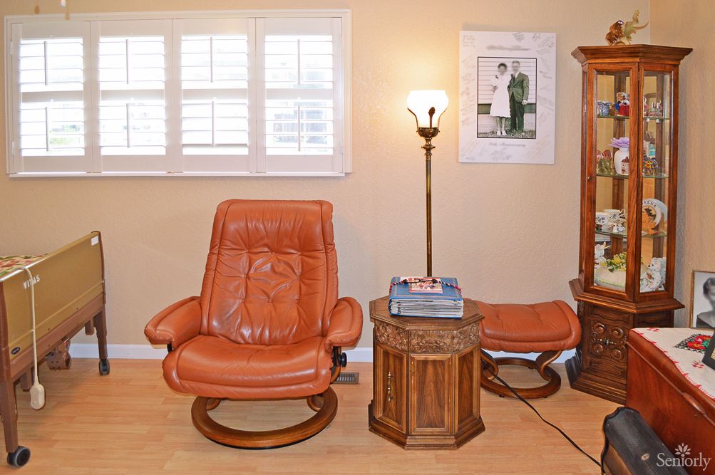 A cozy living room setup featuring a leather chair, side table with books, and a floor lamp next to a window.