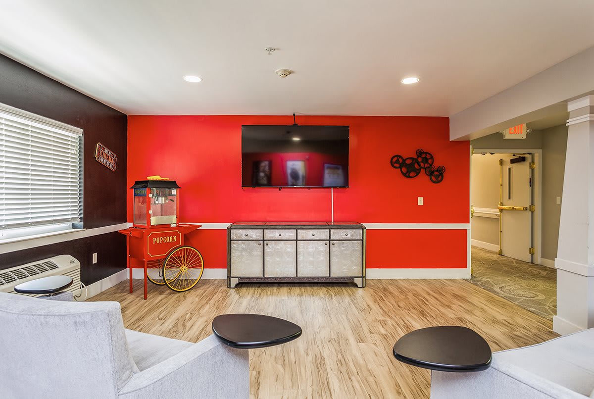 A modern living room entertainment area with a vibrant red accent wall, featuring a large TV and a vintage popcorn machine.