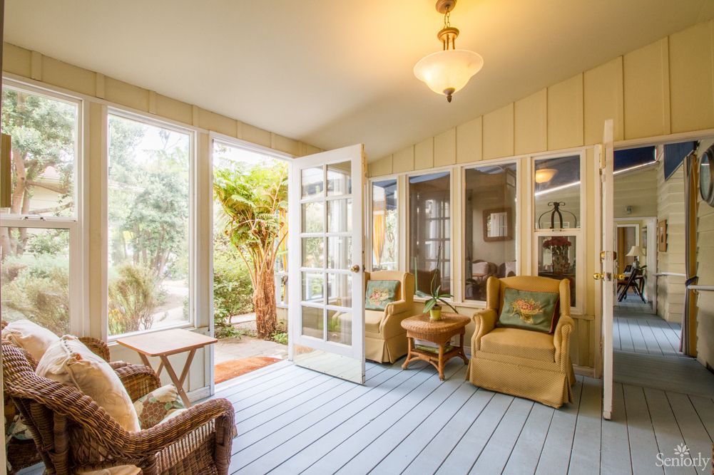 A bright and cozy sunroom featuring comfortable seating and large windows letting in natural light.