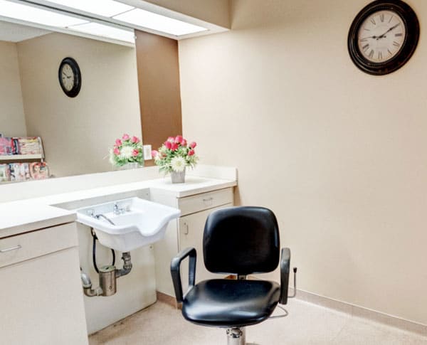 A modern salon setup with a chair, sink, and mirror under soft lighting.