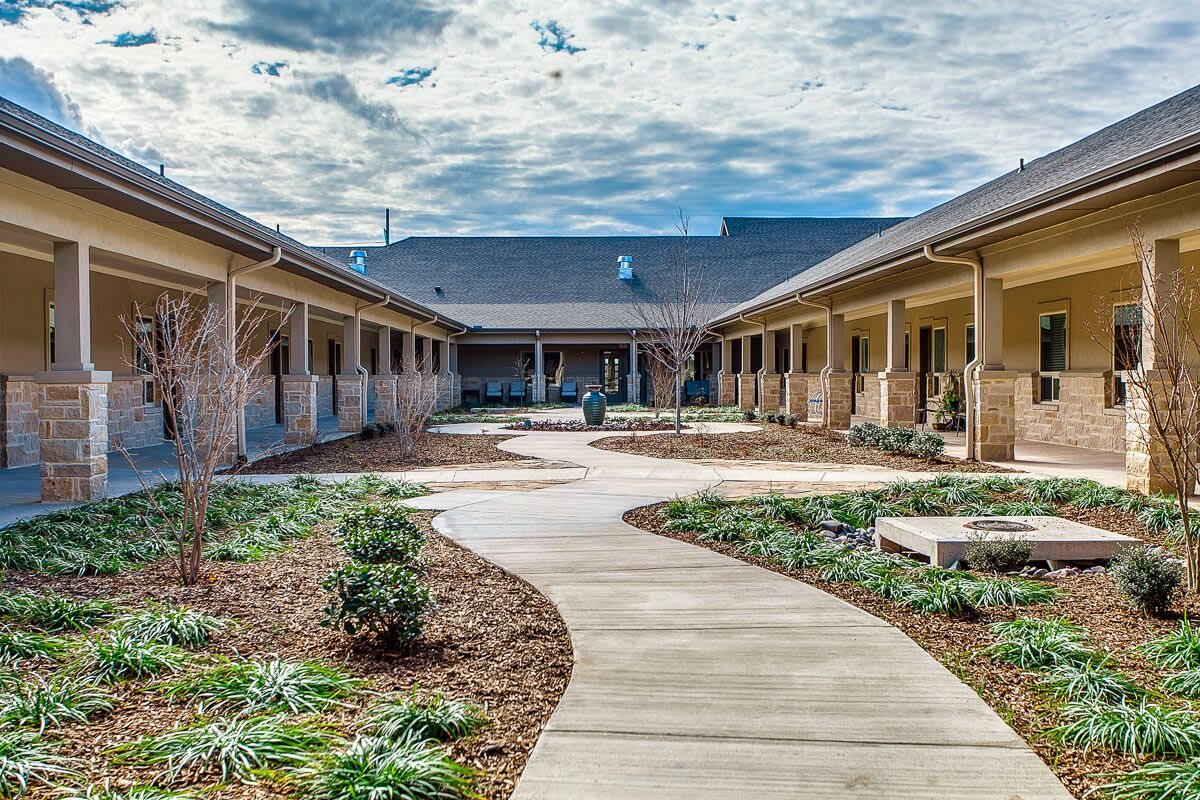 A serene courtyard with a curved pathway and landscaping under a partly cloudy sky.