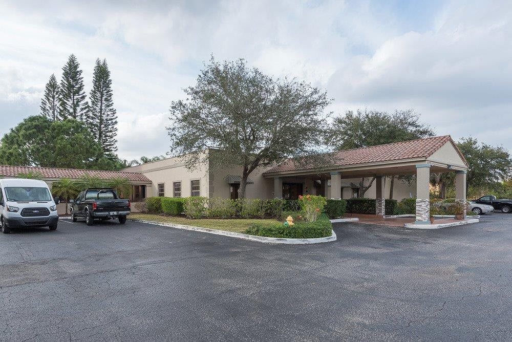 A single-story building with a parking lot and trees on a cloudy day.