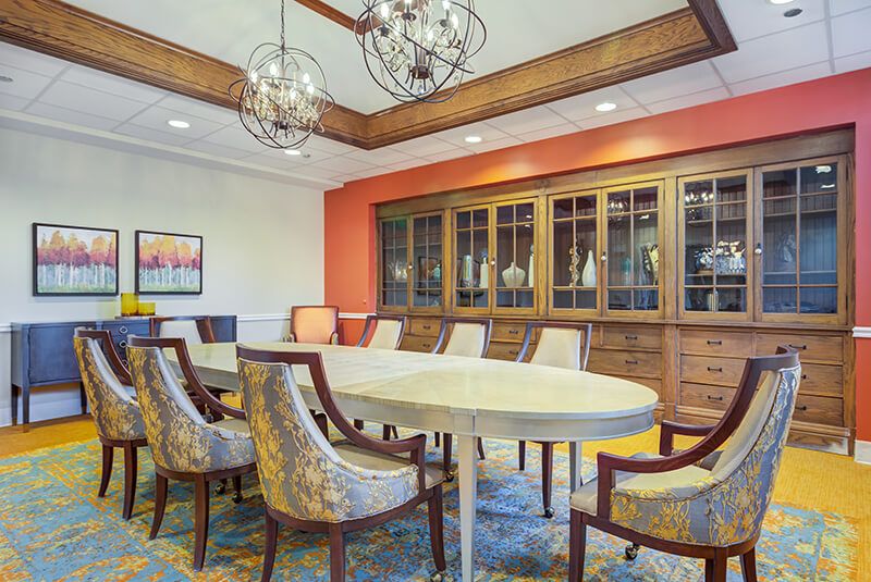 A stylish dining or meeting room with a long oval table, cushioned chairs, and decorative chandeliers.