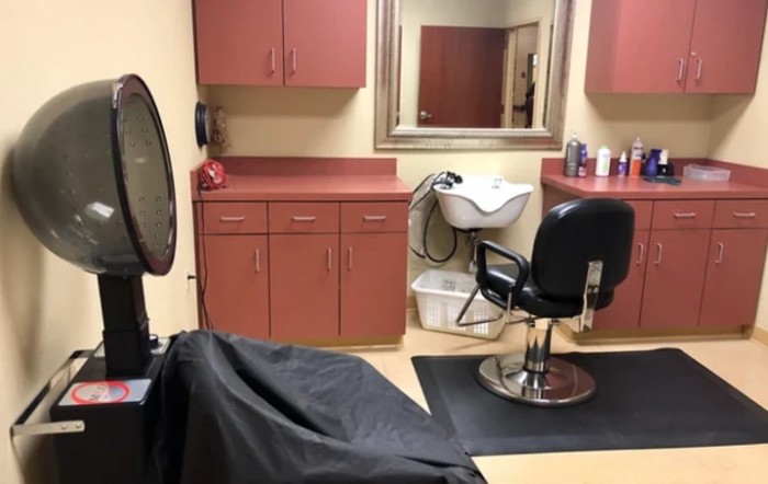 A hair salon interior featuring a styling chair, a sink for washing hair, and cabinets for storage.