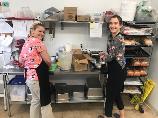 Two women smiling while preparing food in a kitchen.