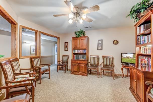 A cozy waiting room with wooden chairs and a bookshelf under a ceiling fan.