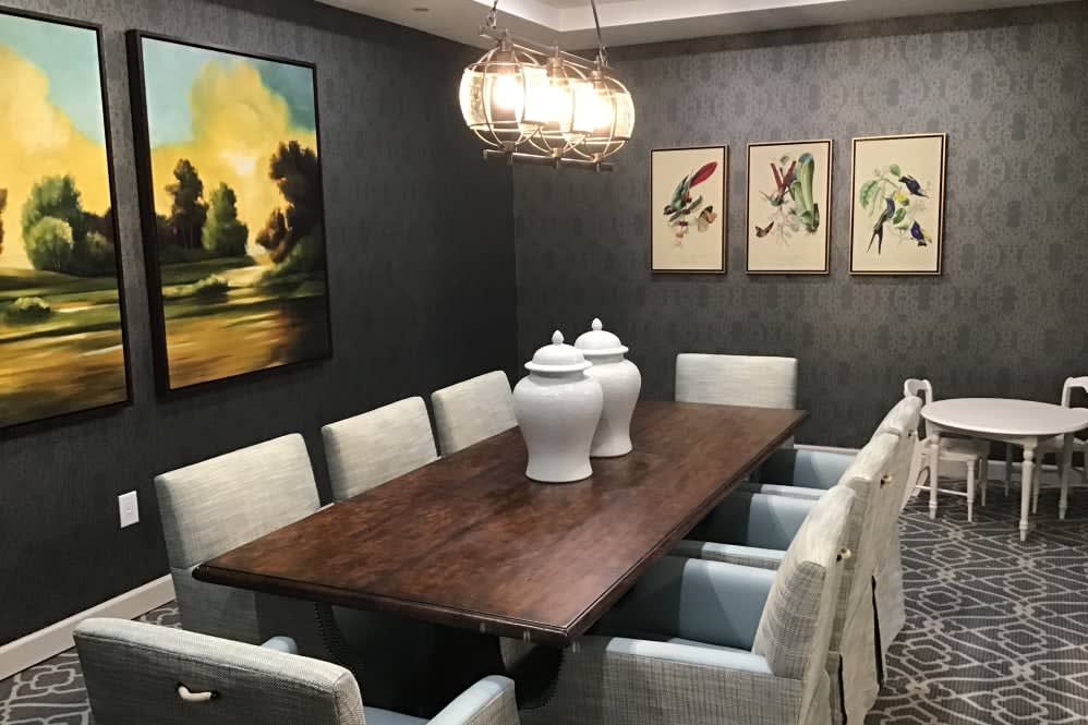 A modern dining room with a wooden table, upholstered chairs, decorative jars, and framed artwork.