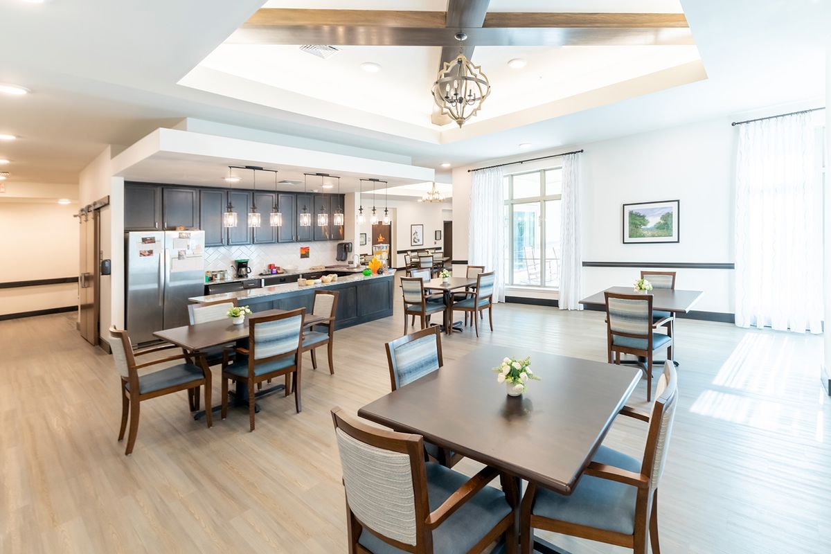 A modern dining area with multiple tables and chairs, featuring a kitchen and elegant lighting.