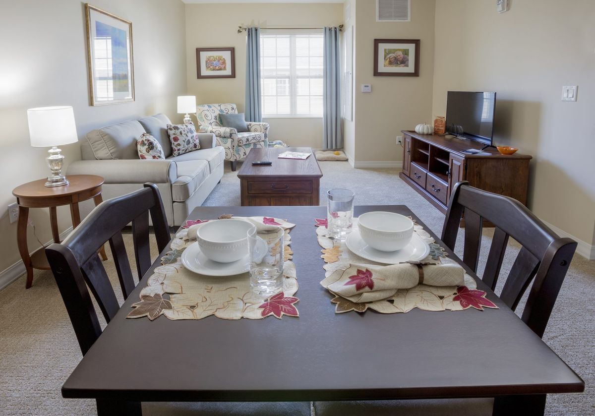 A cozy living room featuring a dining table set for two, with a comfortable sofa and entertainment center.