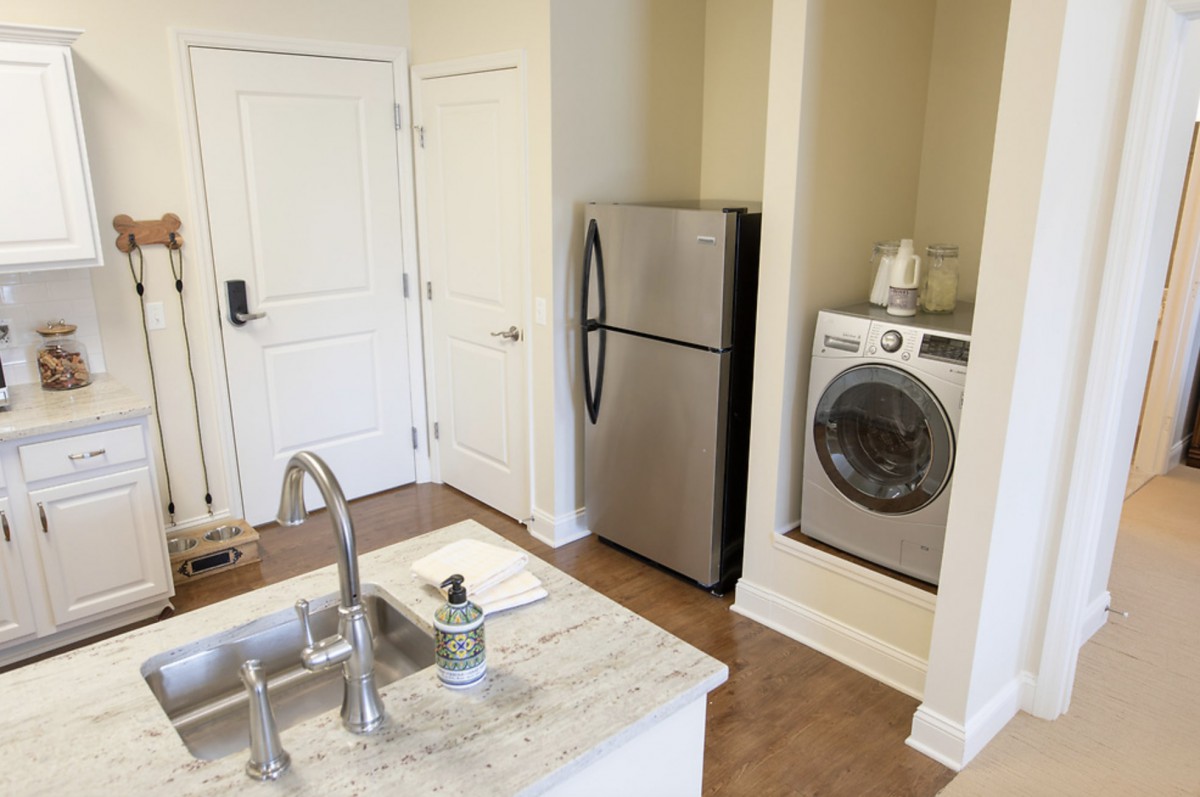 A modern apartment kitchen with a stainless steel fridge and washing machine.