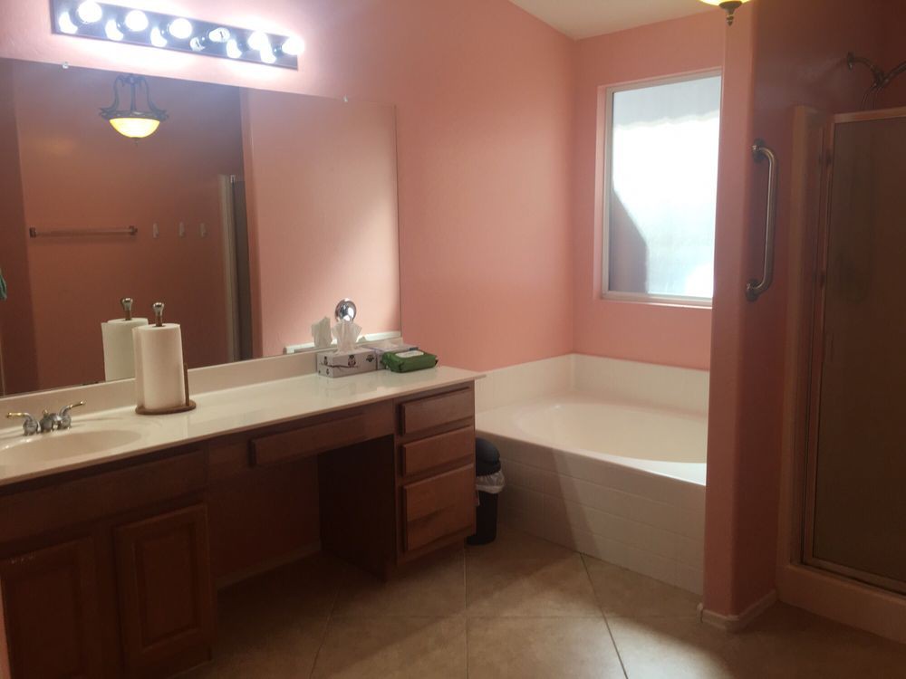 A bathroom with pink walls, featuring a large vanity with a mirror and sink next to a bathtub.