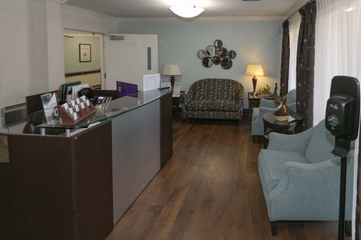 A cozy waiting room with a reception desk, sofas, chairs, and warm lighting.