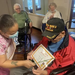A caregiver presents an award to an elderly veteran in a nursing home setting.