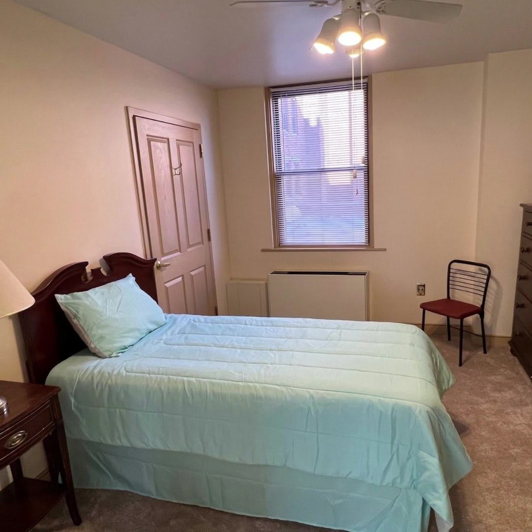 A cozy bedroom with a single bed, window, and wooden furniture.