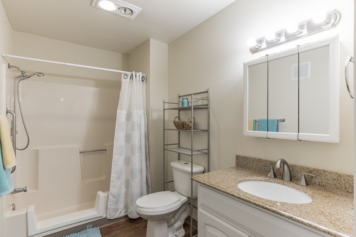 A modern bathroom with a shower, toilet, and sink, featuring a mirror and storage rack.