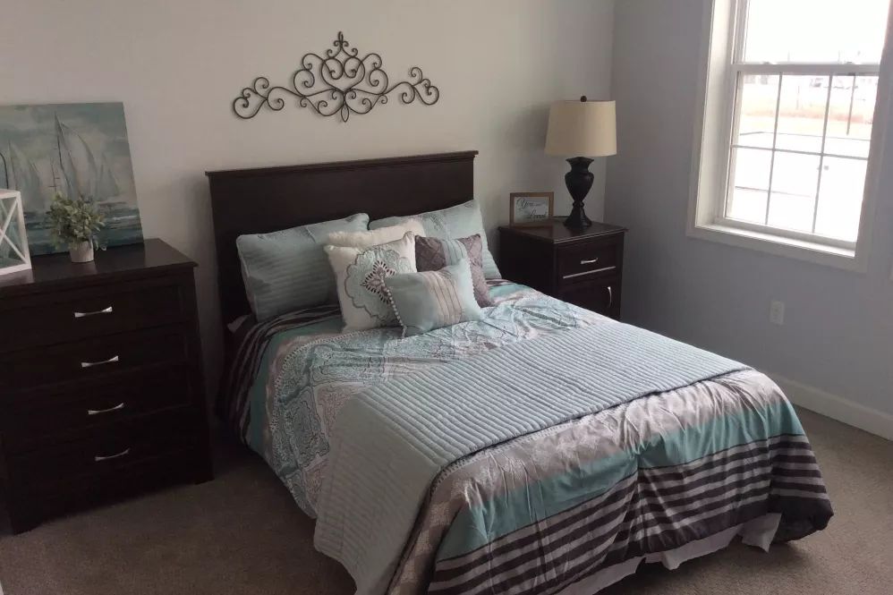 A neatly made bed with decorative pillows in a cozy bedroom, featuring a nightstand and lamp by the window.
