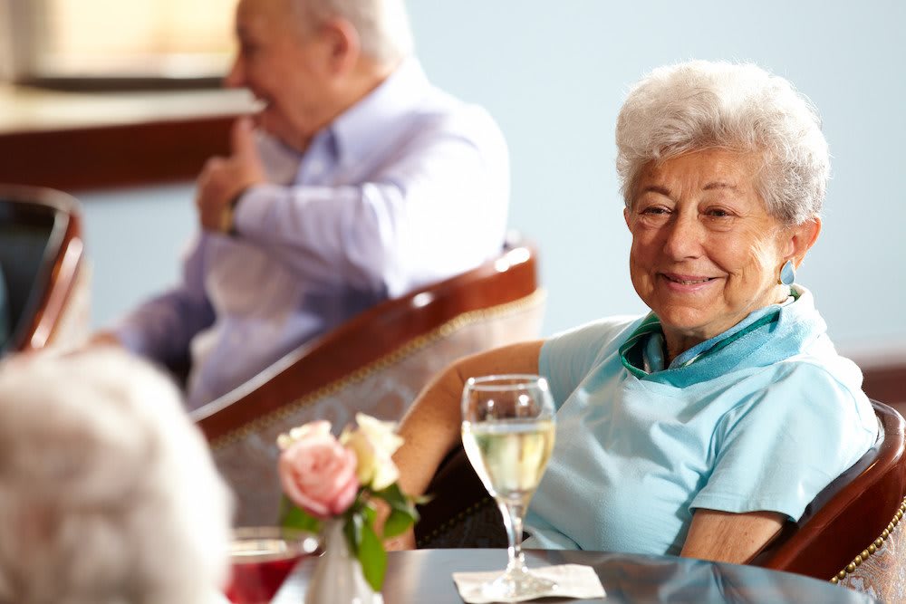 Elderly woman enjoying a social gathering with a glass of wine.