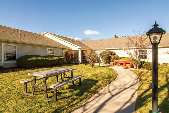 A house with a spacious yard, featuring a picnic table, pathway, and bench under a clear blue sky.