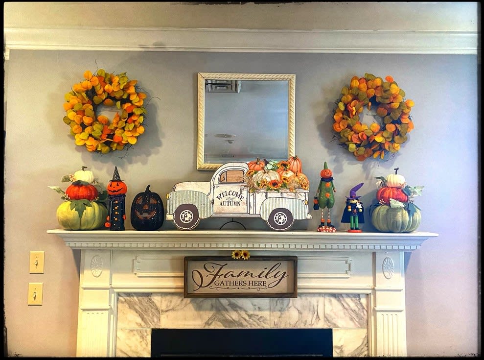A beautifully decorated mantel featuring autumn-themed wreaths, pumpkins, and a vintage truck adorned with seasonal accents.