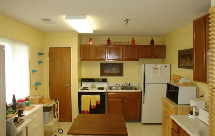 A small apartment kitchen with wooden cabinets, a refrigerator, stove, sink, and microwave.