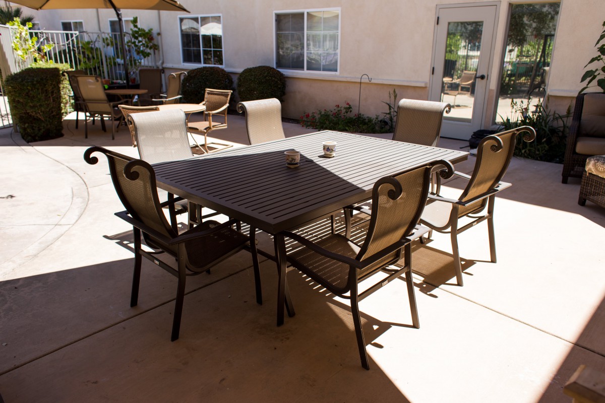A sunny backyard patio with a table and several chairs.
