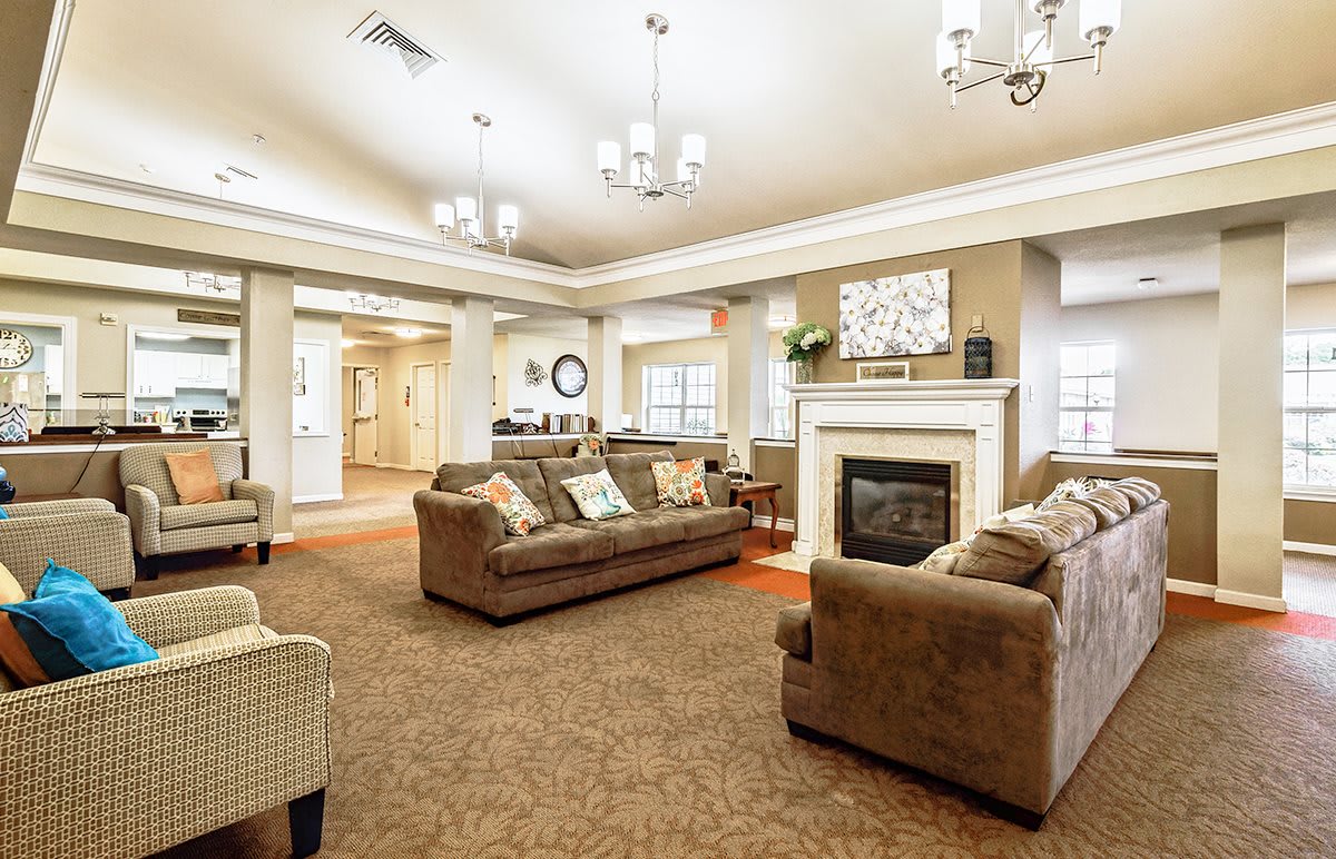 A spacious and elegantly designed living room with comfortable sofas and a fireplace, adorned by chandeliers and tasteful decor.