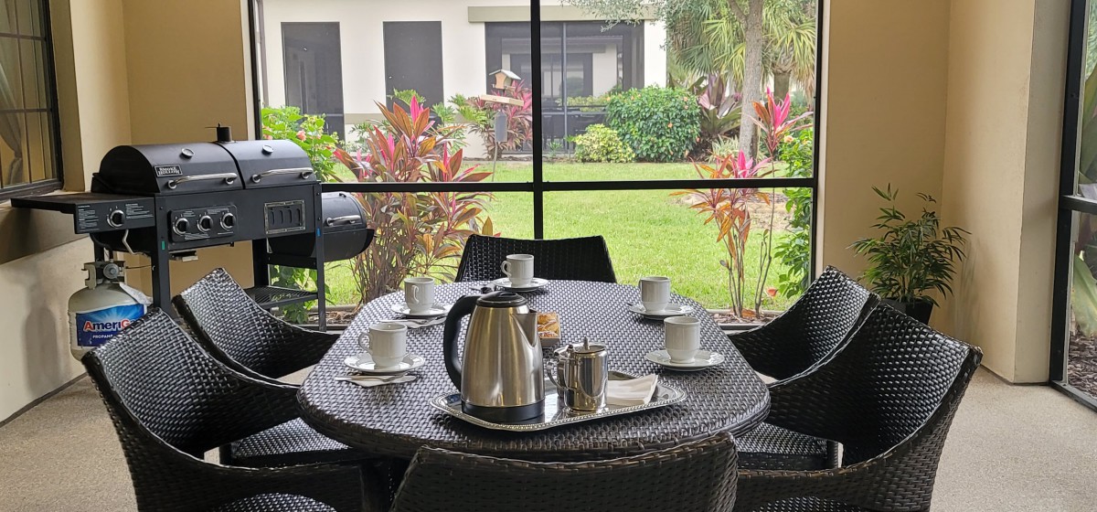 A patio setup with a table featuring coffee cups and a teapot, overlooking a garden.