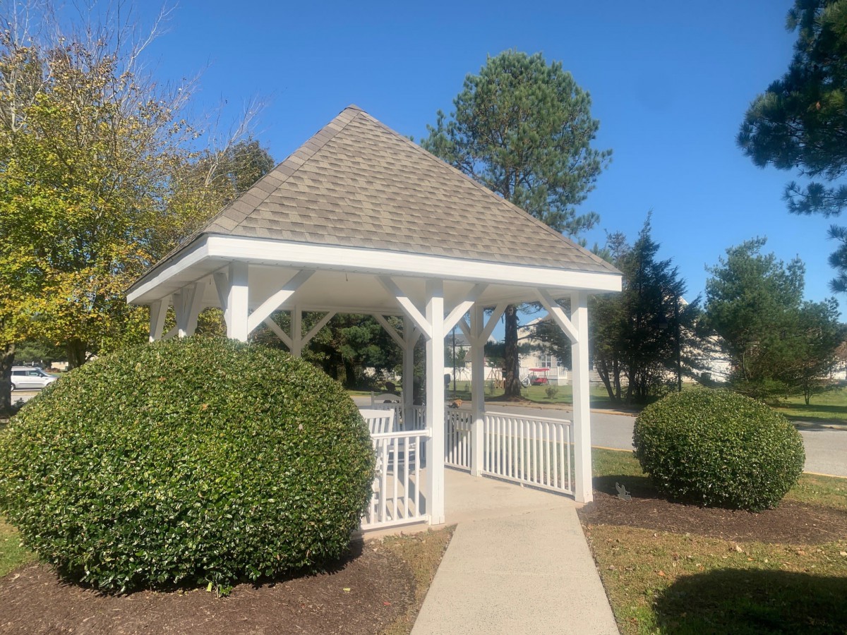 A charming white gazebo set in a landscaped garden under a clear blue sky.