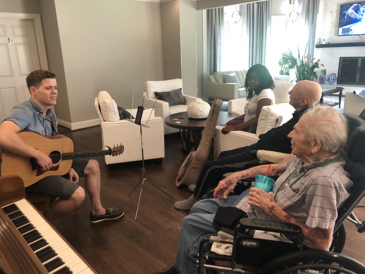 A person playing guitar for an audience of elderly individuals in a cozy room.