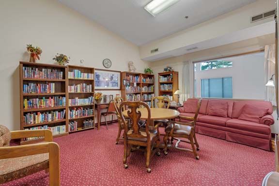 A cozy library room with bookshelves, a round table, chairs, and a comfortable sofa.
