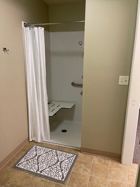 A bathroom with a shower stall featuring a curtain, shower seat, and grab bar.