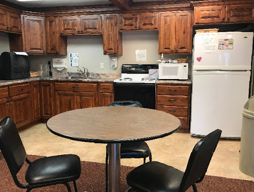 A cozy kitchen featuring a round table and black chairs, surrounded by wooden cabinets and essential appliances.