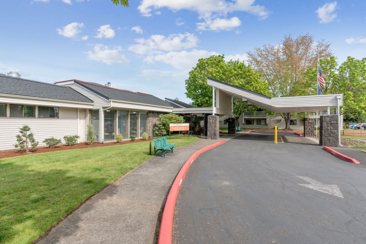 A view of a building entrance with a driveway and landscaped surroundings.