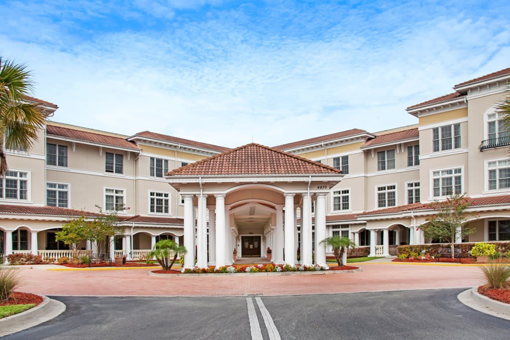 A large residential building with a grand entrance featuring columns and neatly landscaped surroundings.