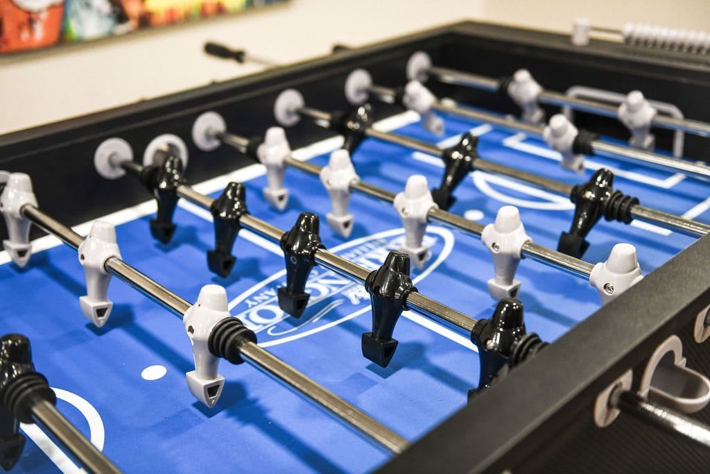 A close-up view of a foosball table with black and white player figures on a blue playing field.