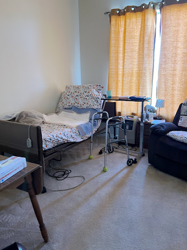 A cozy home setup featuring a hospital bed, comfortable chair, and warm yellow curtains.