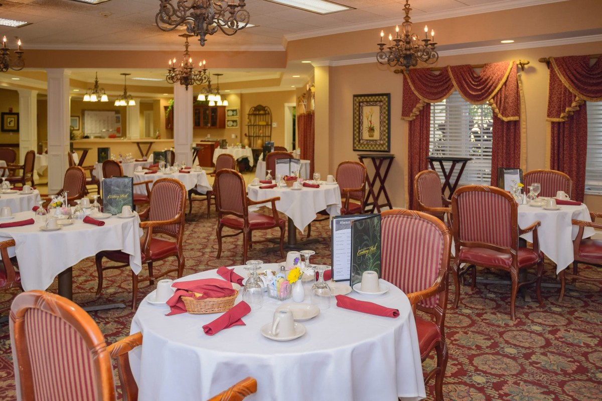 An elegant dining room with neatly set tables and chandeliers.
