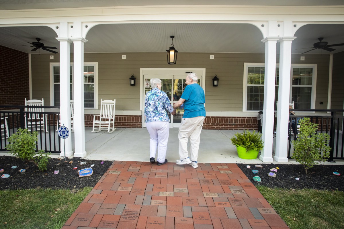 Two elderly individuals walking together towards a home's entrance, showcasing companionship and support.